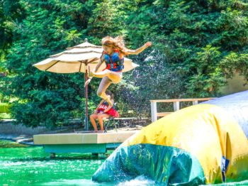 A camper jumping off a blob in the lake.