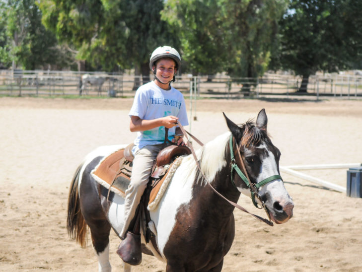 A camper smiling while on a horse.